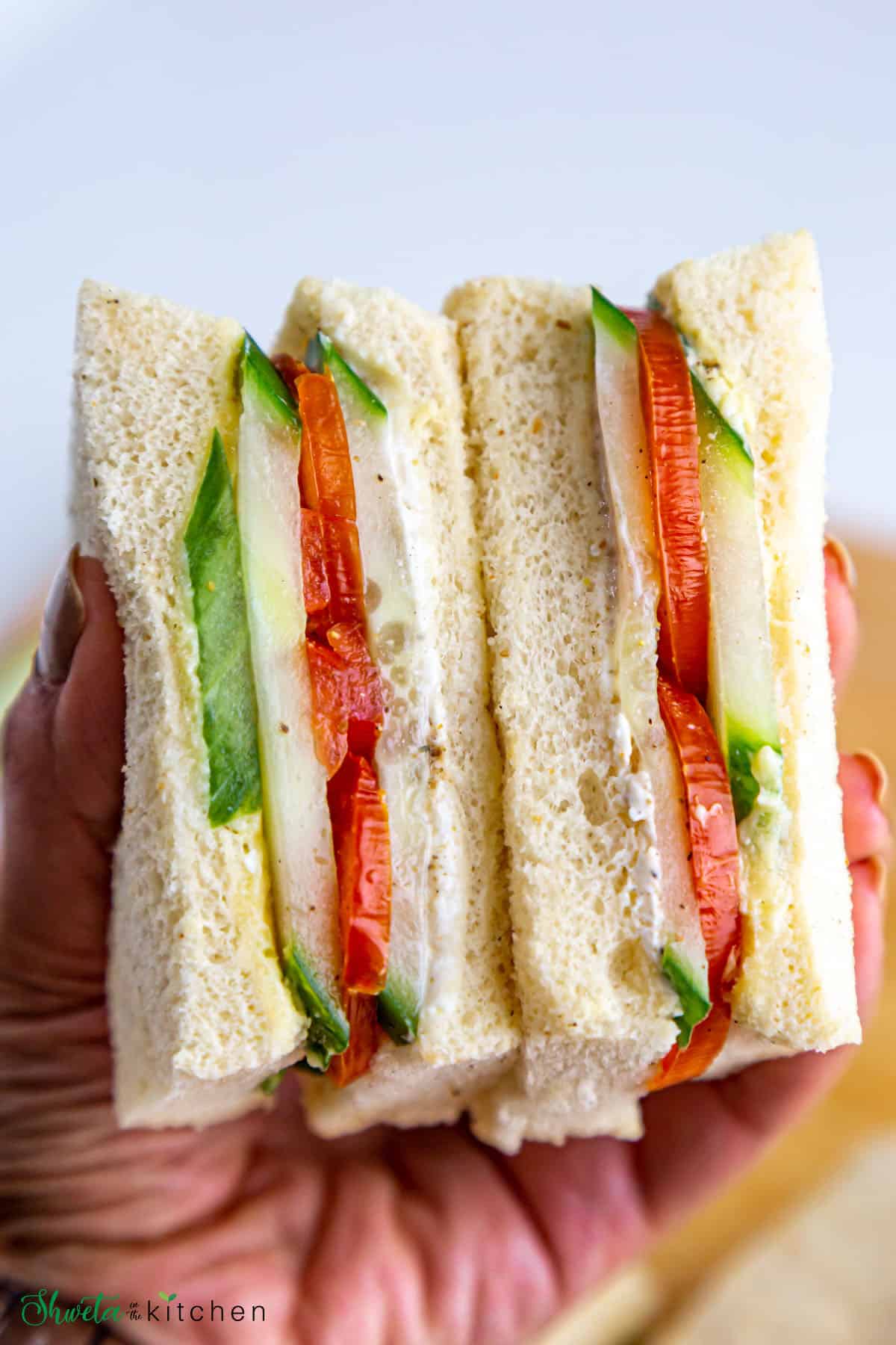 Half cut tomato cucumber sandwich held in hand showing the inside of sandwich