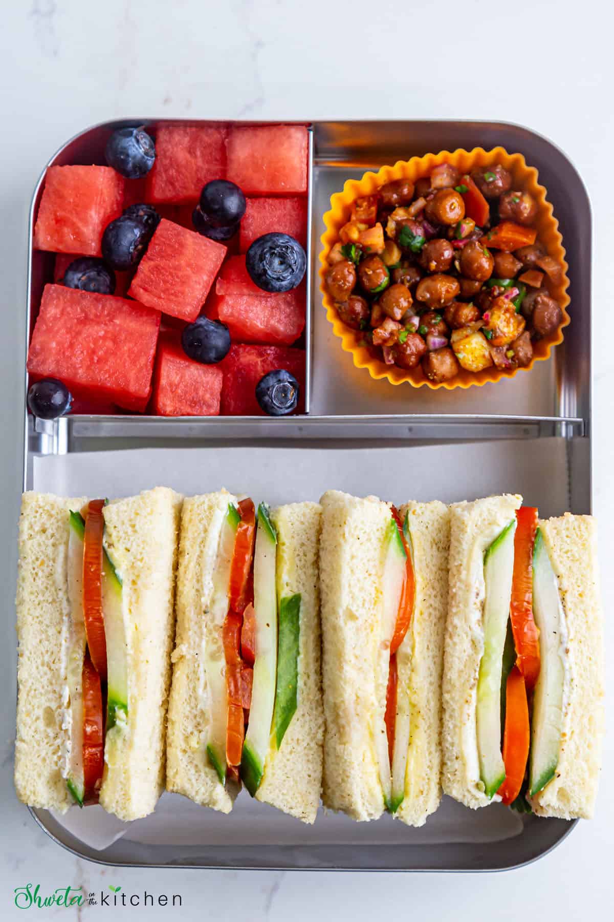 Tomato cucumber sandwich in stainless steel lunchbox with chickpea salad and fruits