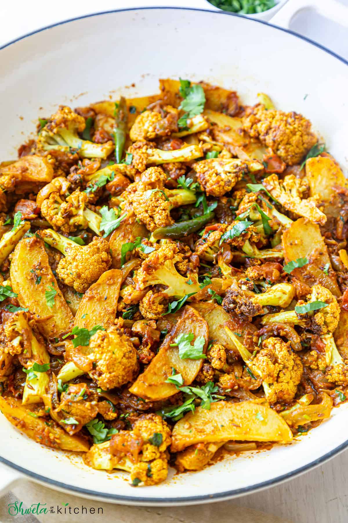 Side view of vegan aloo gobi (potato and cauliflower curry) on a pan
