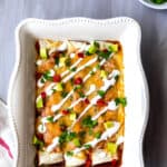Vegetarian enchiladas in a white baking dish drizzled with sour cream