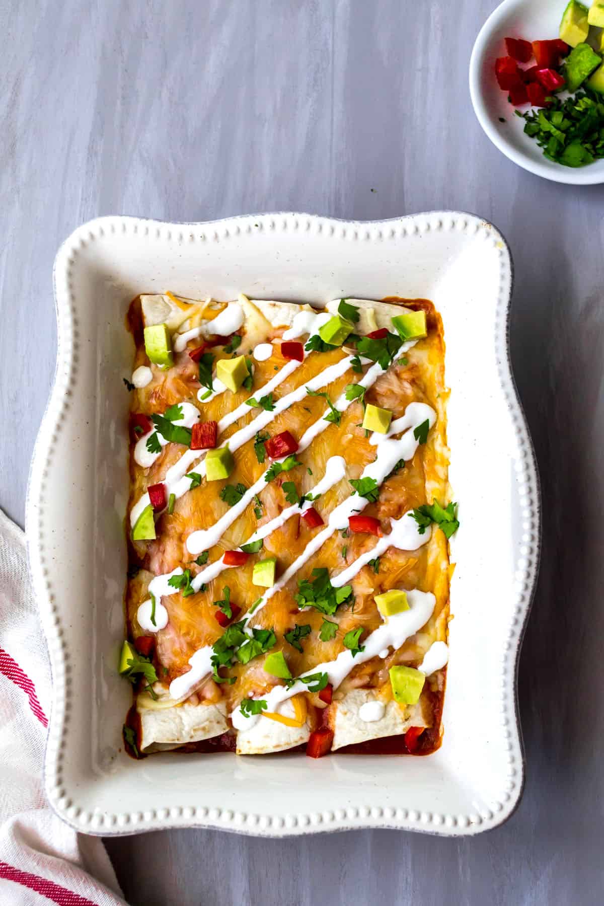 Vegetarian enchiladas in a white baking dish drizzled with sour cream