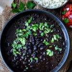 Top view of Instant Pot Mexican black beans in a black bowl garnished with cilantro with rice on the side