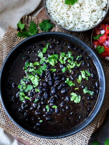 Top view of Instant Pot Mexican black beans in a black bowl garnished with cilantro with rice on the side