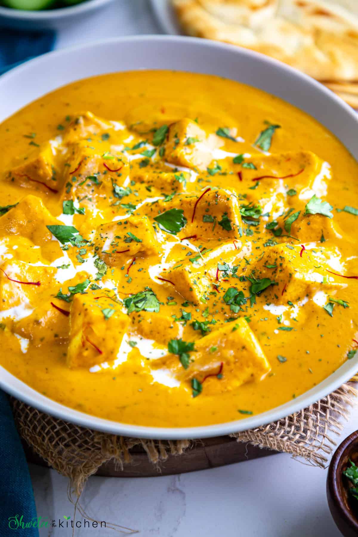 Side view of bowl of shahi paneer garnished with cilantro, saffron and cream