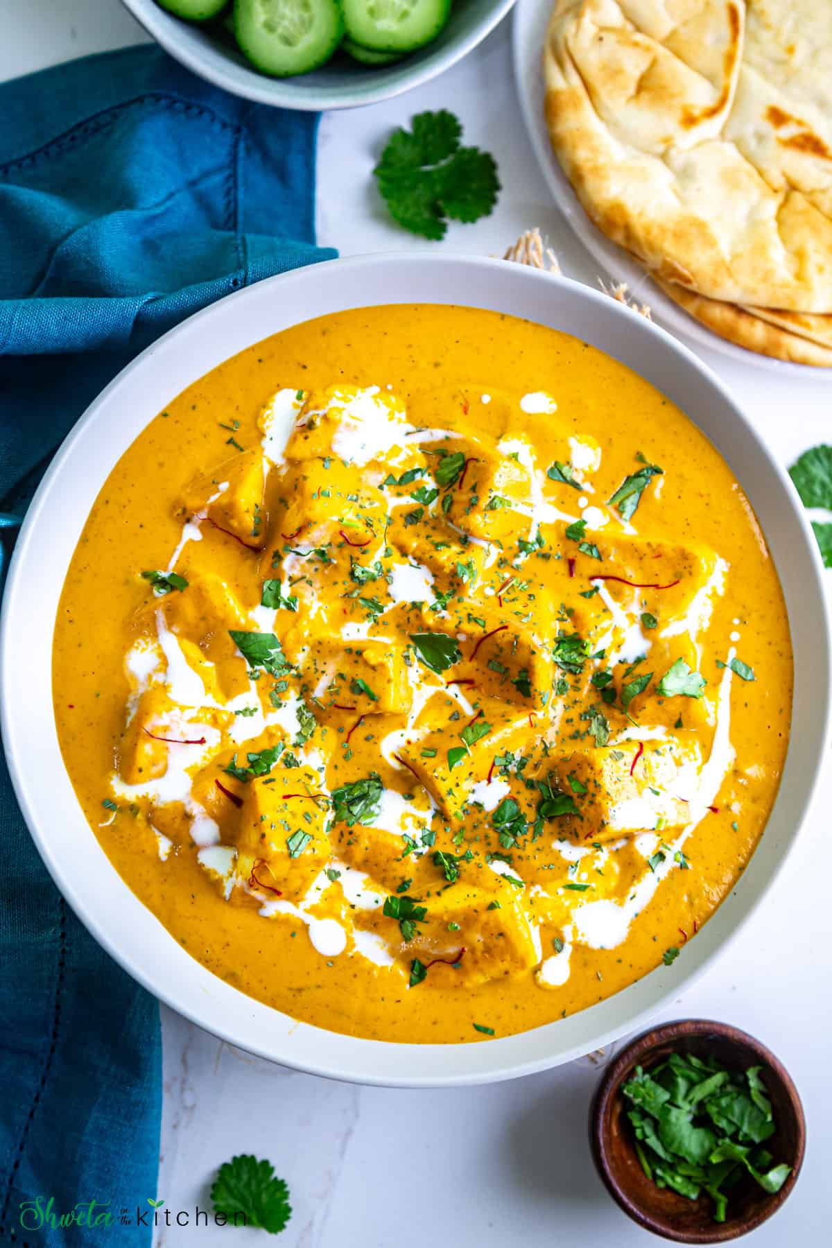 Top view of bowl of shahi paneer garnished with cilantro, saffron and cream 