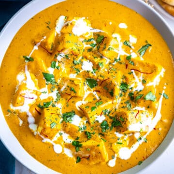 Top view of bowl of shahi paneer garnished with cilantro, saffron and cream