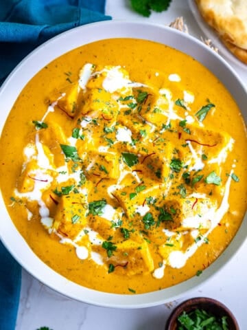 Top view of bowl of shahi paneer garnished with cilantro, saffron and cream