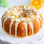 Side view of eggless orange cake drizzled with orange glaze, and garnished with sliced almonds